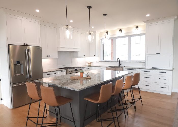 A white and grey custom kitchen with tall cabinetry and granite countertops, with a large window over the sink.